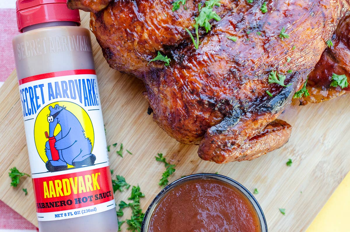Aardvark hot sauce bottle next to a roasted chicken on a wooden cutting board.