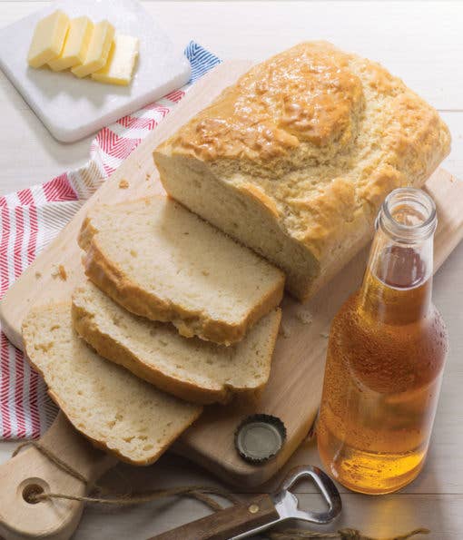 Loaf of bread with slices on a cutting board next to a bottle of beer.