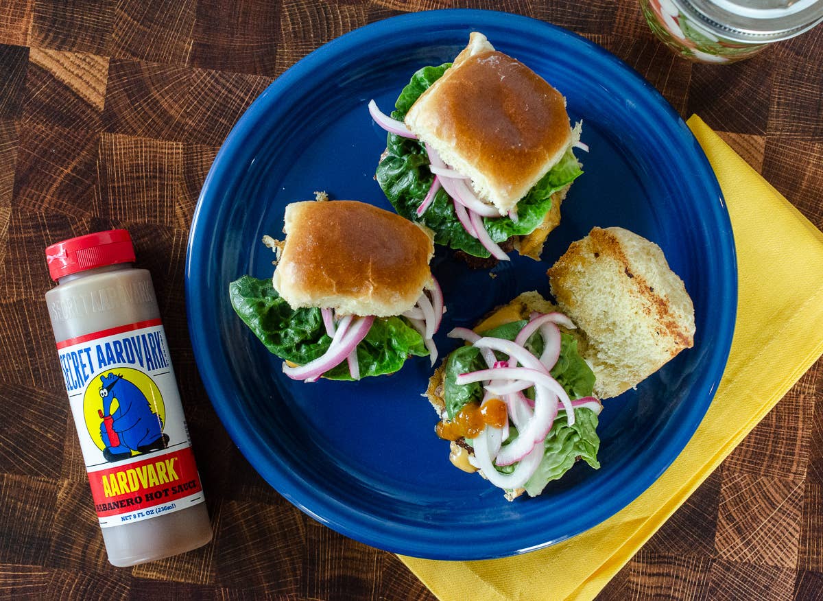 Blue plate with sliders, a bottle of Aardvark hot sauce on a wooden surface