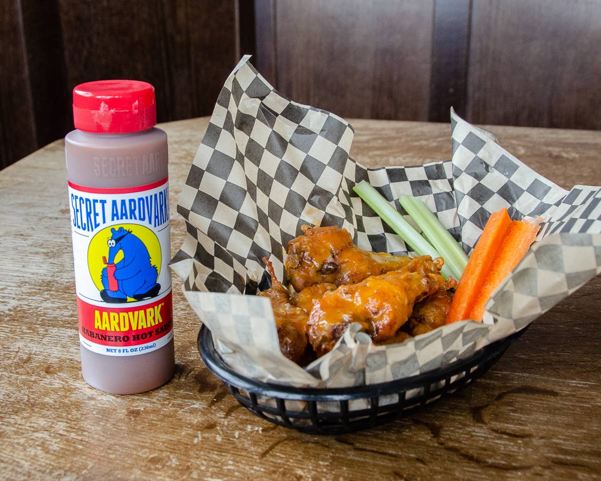 Bowl of wings with carrots and celery, accompanied by a bottle of Secret Aardvark sauce on a wooden table.