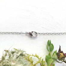 Load image into Gallery viewer, Close-up of a silver clasp on a chain with a natural background of green plants.
