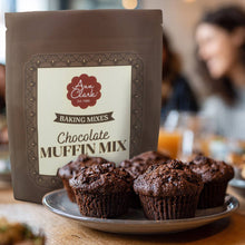 Load image into Gallery viewer, Bag of Ann Clark Chocolate Muffin Mix with muffins on a plate in a blurred cafe setting
