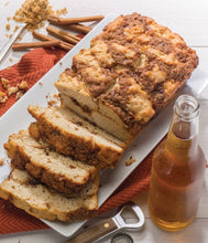 Load image into Gallery viewer, Loaf of bread with slices cut, next to a bottle of beer on a wooden surface.
