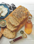 Loaf of bread with slices on a wooden board, accompanied by a bottle of beer and condiments.