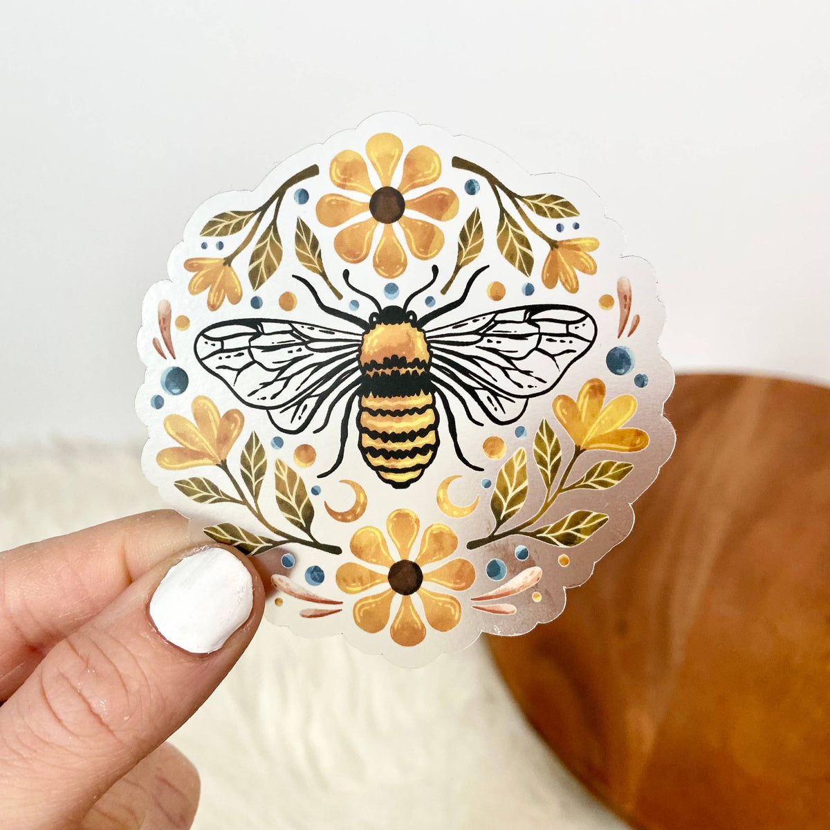 Decorative sticker with a bee and flowers held by a hand on a neutral background