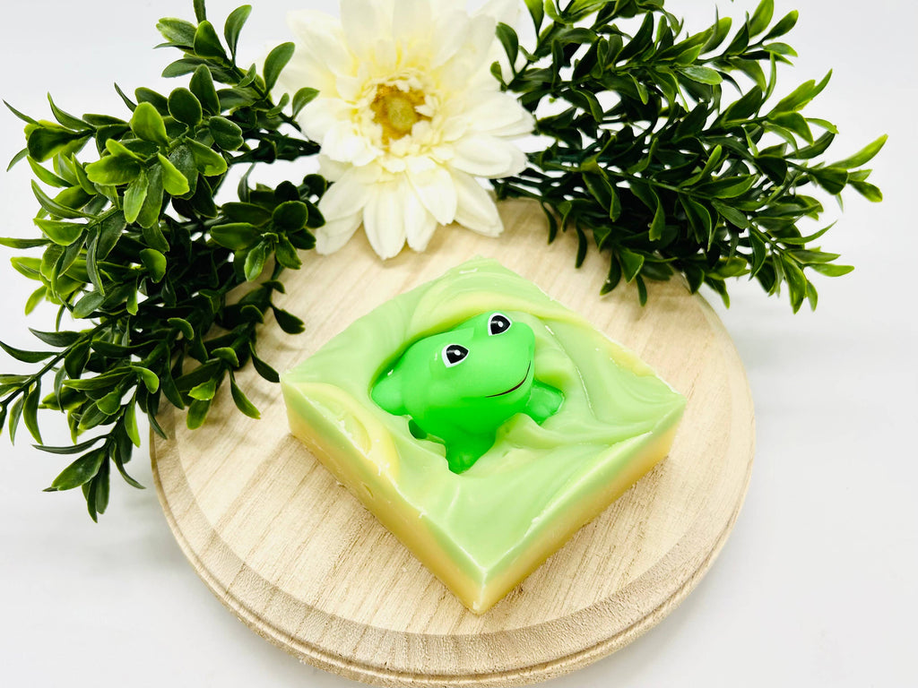 Green frog-shaped soap on a wooden board with flowers and leaves