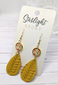 Mustard yellow leaf-shaped earrings with floral accents on a 'Starlight Story' branded card.