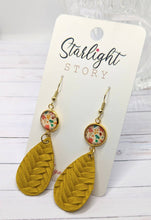 Load image into Gallery viewer, Mustard yellow leaf-shaped earrings with floral accents on a 'Starlight Story' branded card.

