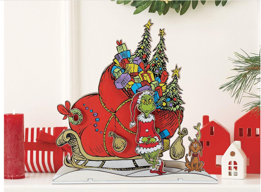 Illustration of the Grinch with a sleigh full of presents and a dog in a Christmas scene.
