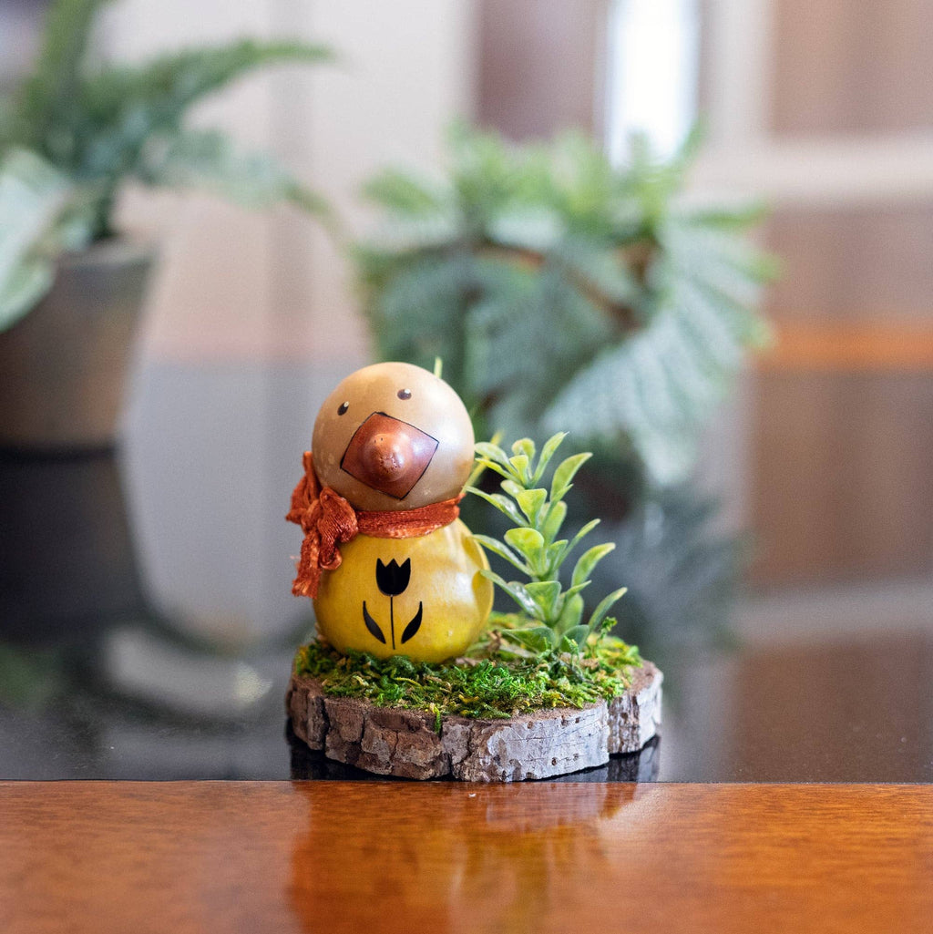 Decorative figurine of a duck with a red scarf on a wooden surface with plants in the background