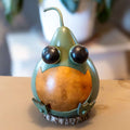 Decorative gourd with googly eyes and a smiling mouth on a wooden surface.