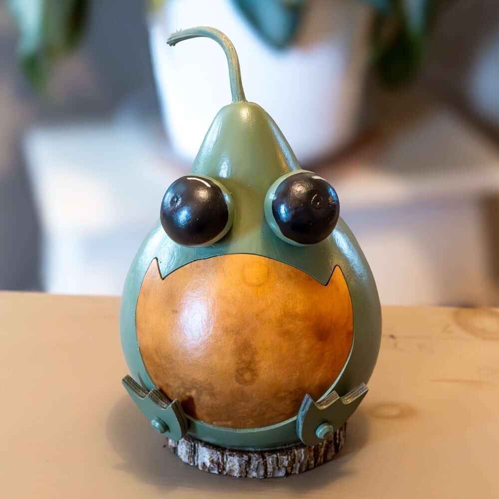 Decorative gourd with googly eyes and a smiling mouth on a wooden surface.