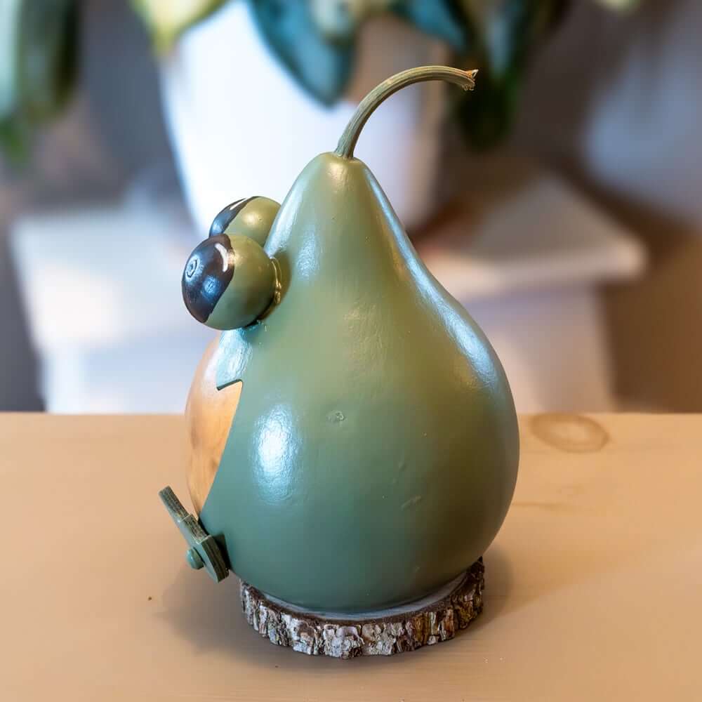 Green pear-shaped object with a face on a wooden surface