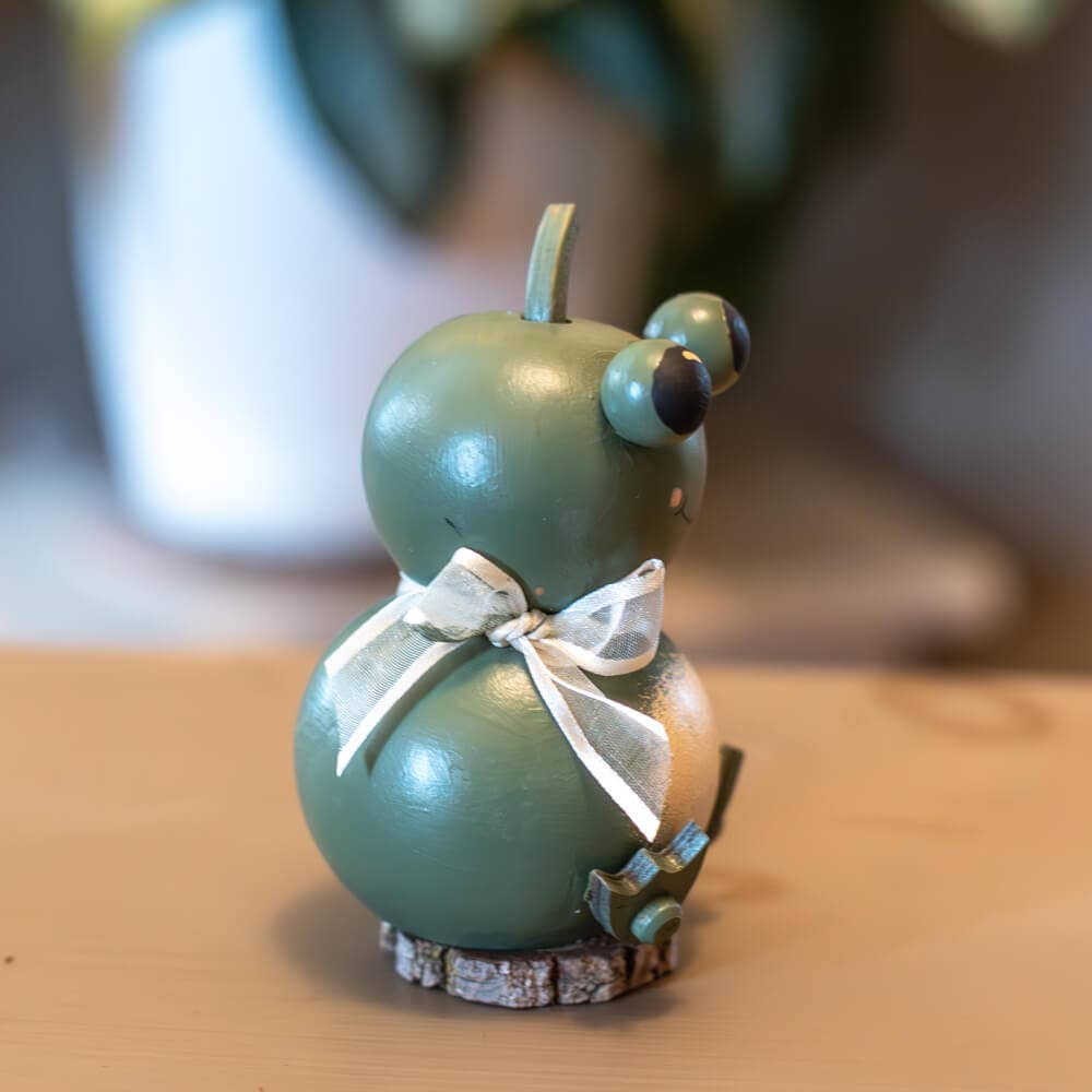 Green decorative gourd with a white ribbon on a wooden surface