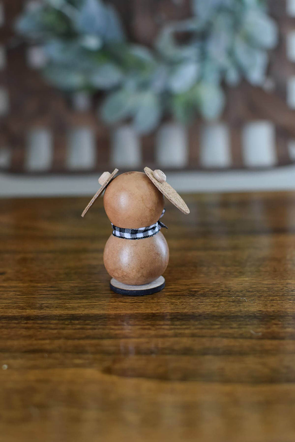 Wooden rabbit figurine with a checkered ribbon on a wooden surface with a blurred plant background
