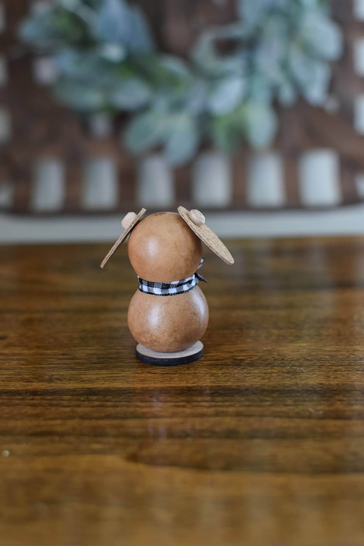 Wooden rabbit figurine with a checkered ribbon on a wooden surface with a blurred plant background