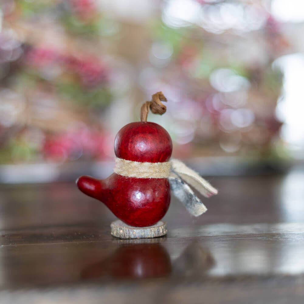 Red birdhouse ornament on a wooden surface with a blurred floral background