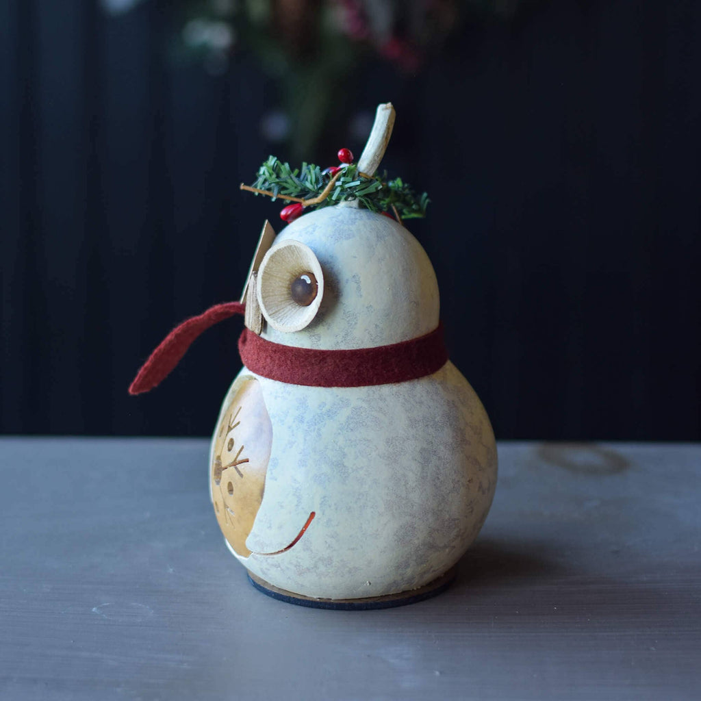 Decorative penguin ornament with a red scarf and greenery on a dark background