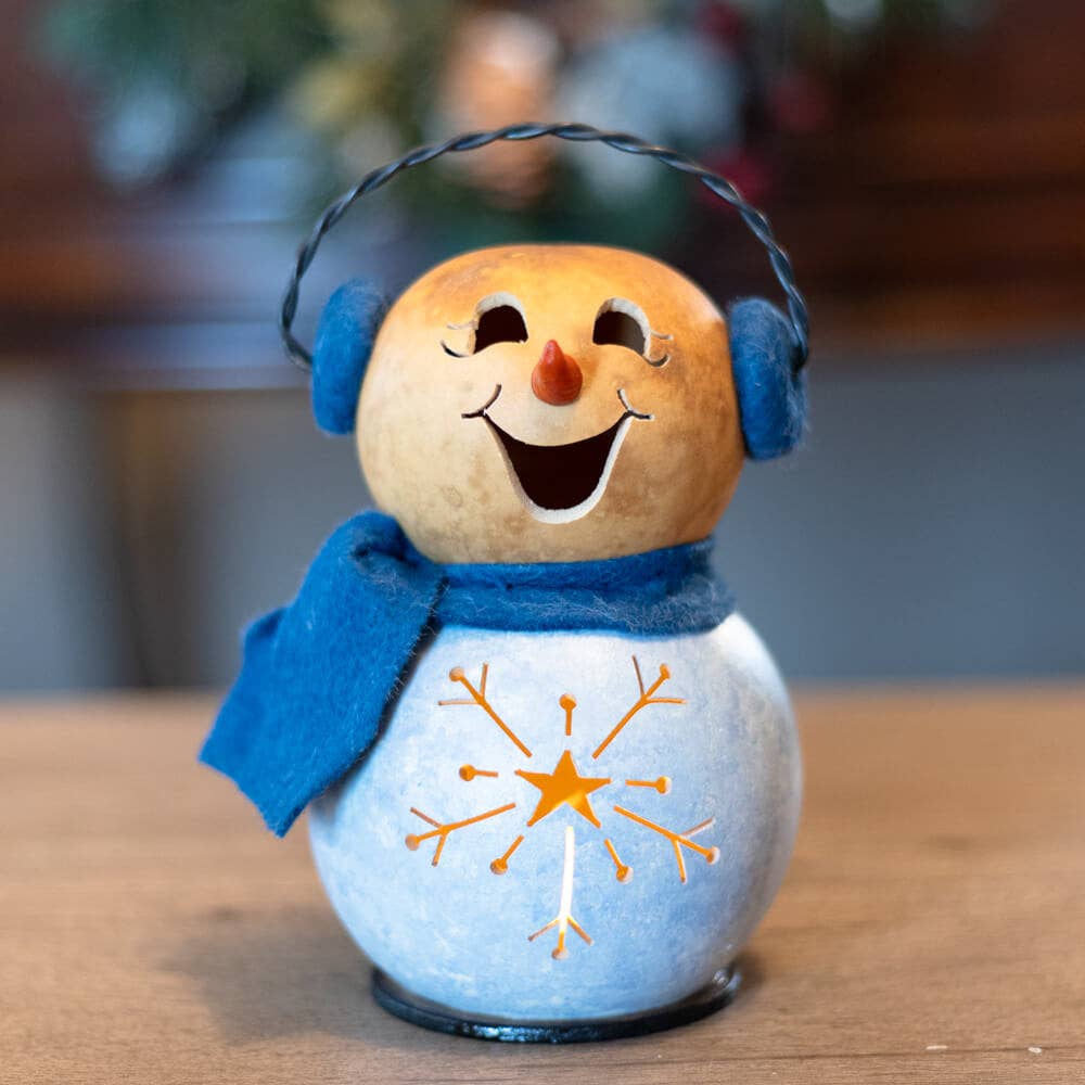 Decorative snowman ornament with a blue scarf and ear muffs on a wooden surface.