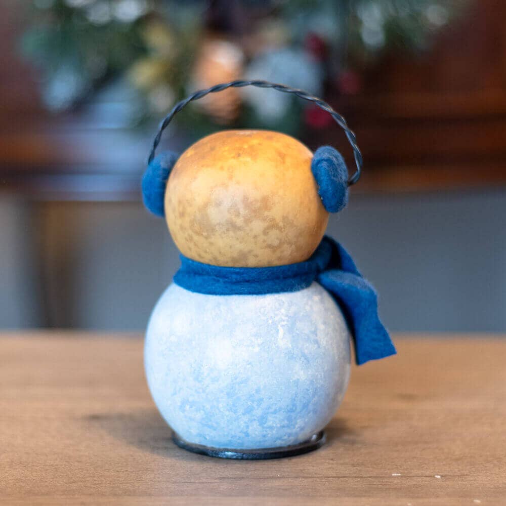 Decorative snowman ornament with blue scarf and earmuffs on a wooden surface.