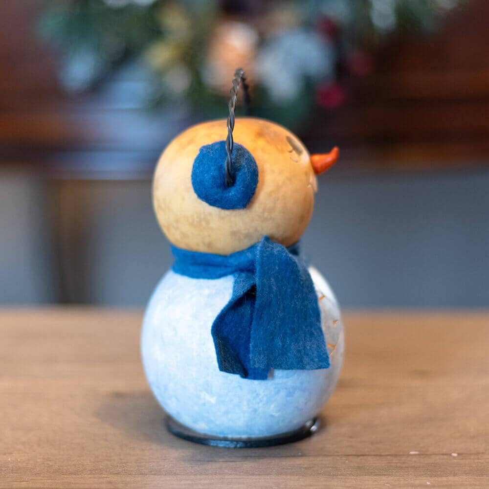 Small snowman decoration with a blue scarf on a wooden surface
