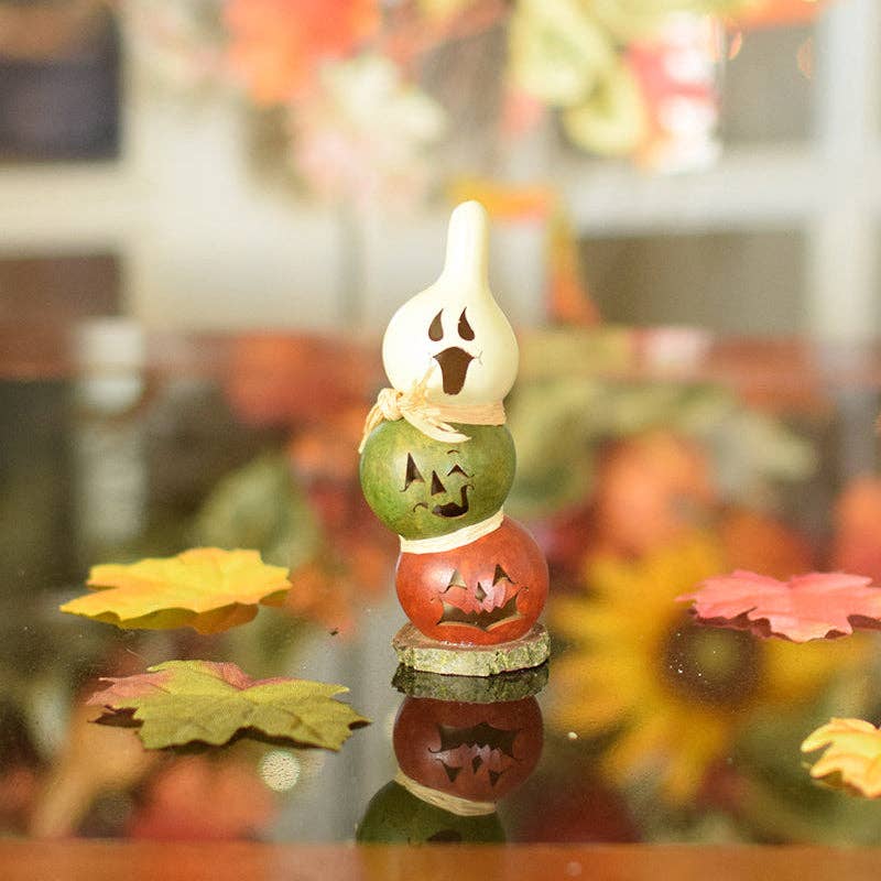 Decorative Halloween candle holder with carved pumpkins on a reflective surface.