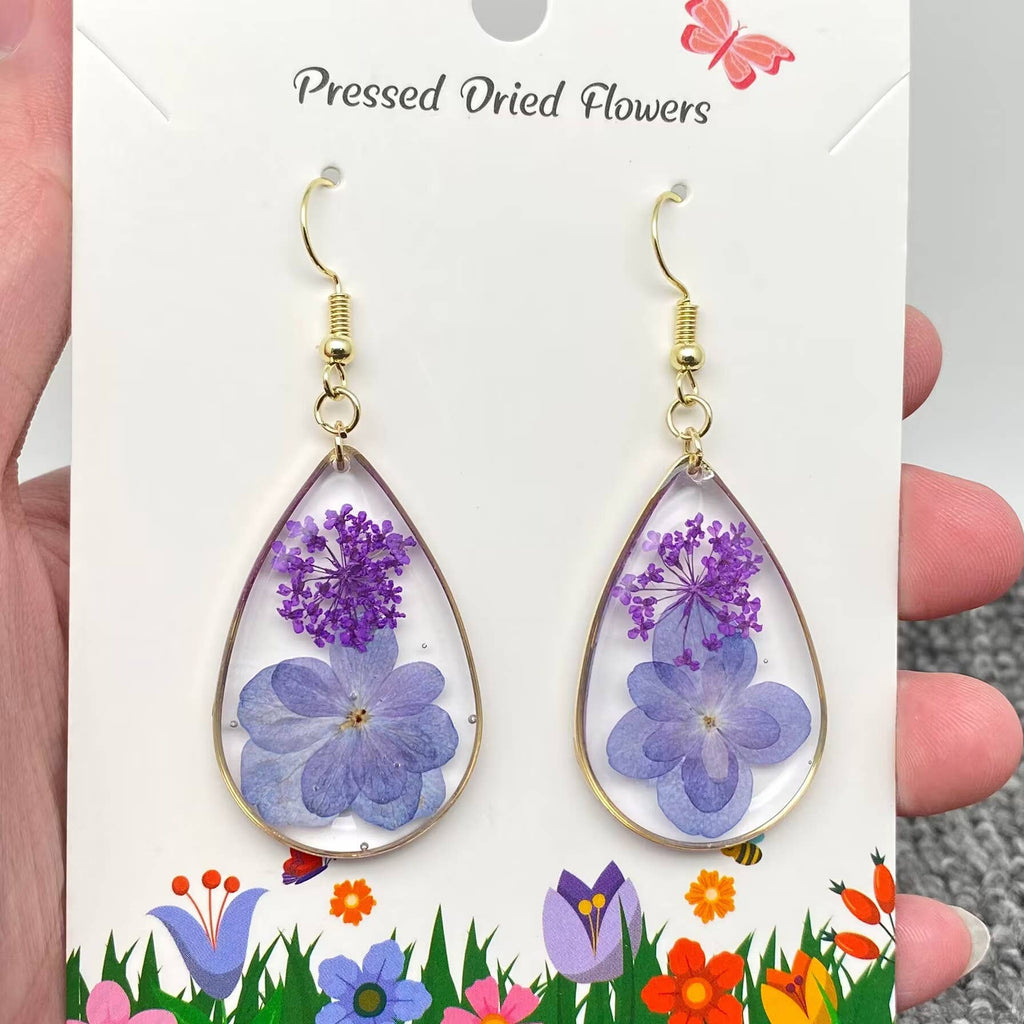 Teardrop-shaped earrings with pressed dried flowers on a card with floral design