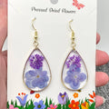 Teardrop-shaped earrings with pressed dried flowers on a card with floral design