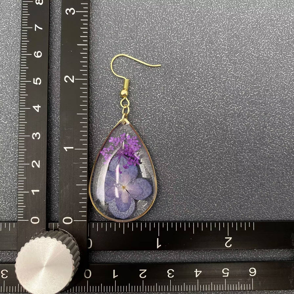 Teardrop-shaped earrings with purple flowers on a ruler for scale