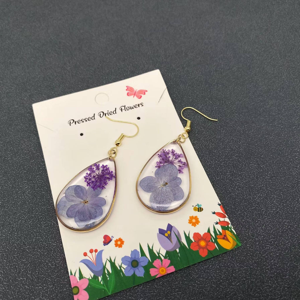 Teardrop-shaped earrings with pressed dried flowers on a decorative card against a dark background