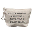 A canvas cosmetic pouch in a light beige color with black printed text that reads 'I'LL STOP WEARING BLACK WHEN THEY INVENT A DARKER COLOR'. It features a white zipper closure at the top and a white drawstring loop on the left side, set against a plain white background.