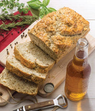 Load image into Gallery viewer, Loaf of bread sliced on a cutting board with a bottle of beer and herbs in the background.
