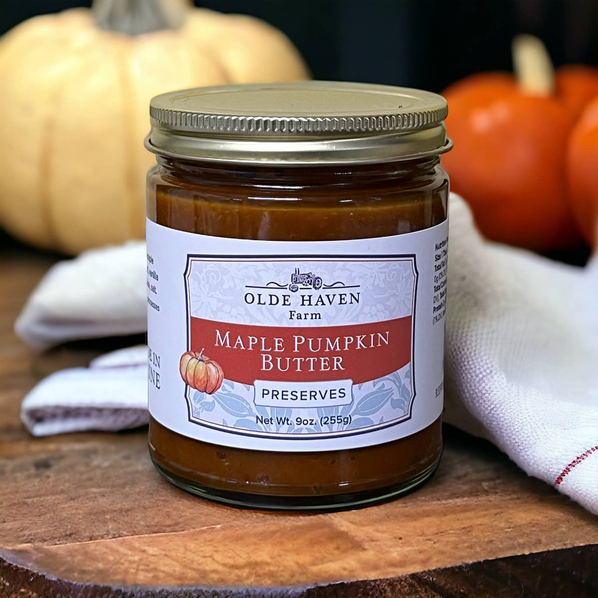 Jar of Olde Haven Farm Maple Pumpkin Butter on a wooden surface with pumpkins in the background