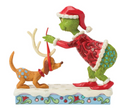 Decorative figurine of a green character in a red outfit and Santa hat interacting with a brown dog with antlers on a white background.