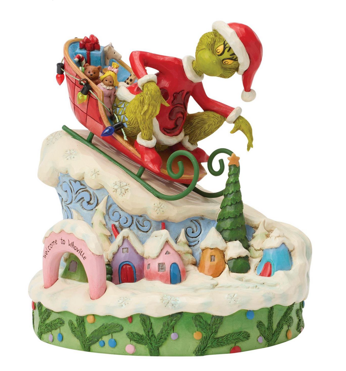 Decorative figurine of a character in a red hat and green suit with a sleigh, set against a snowy village background.