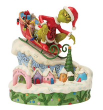 Load image into Gallery viewer, Decorative figurine of a character in a red hat and green suit with a sleigh, set against a snowy village background.
