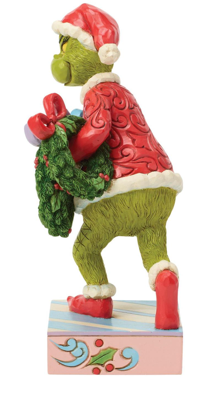 Decorative figurine of a character in a Santa hat and red sweater with a green wreath, on a white background.