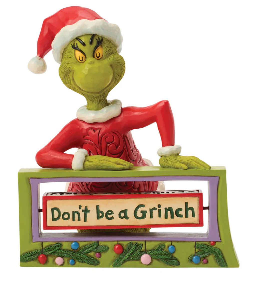 Grinch figurine with 'Don't be a Grinch' sign on a white background