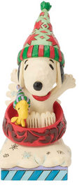 Snoopy figurine wearing a red and green striped party hat and a small green striped hat, sitting in a red bowl with a yellow duckling, on a white background.