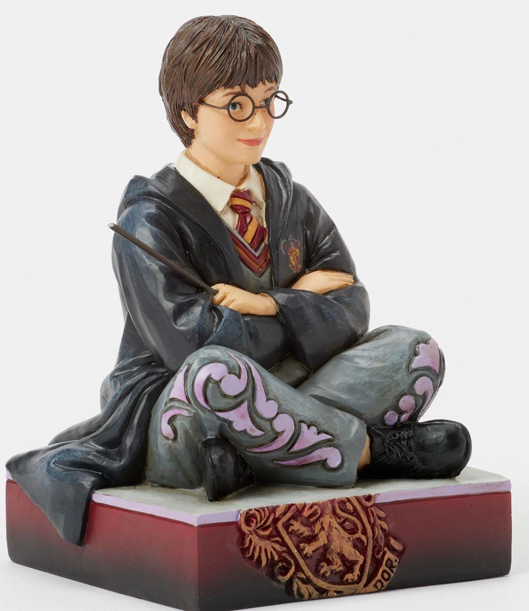 Figurine of a Harry Potter in a gray robe with a wand, sitting on a decorative base.Artist Jim Shore.
