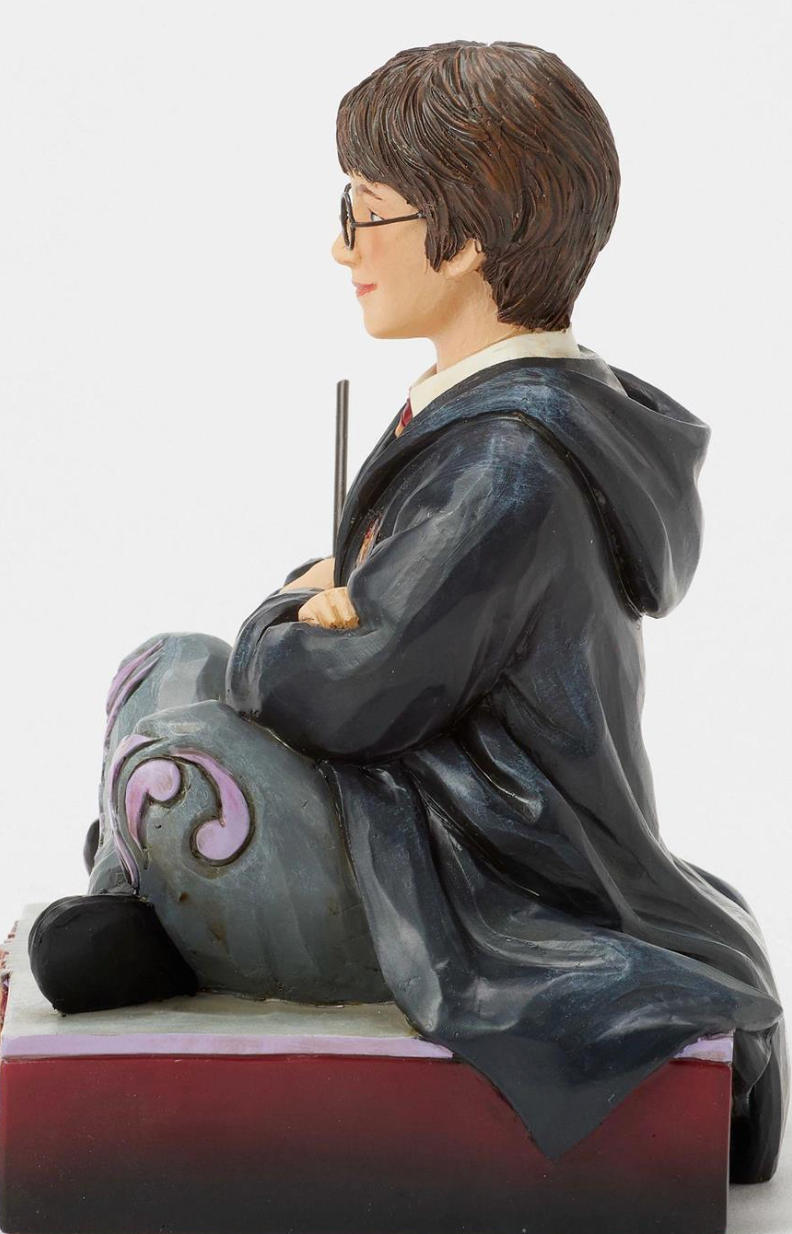 Figurine of a Harry Potter in a gray robe with a wand, sitting on a decorative base.Artist Jim Shore.