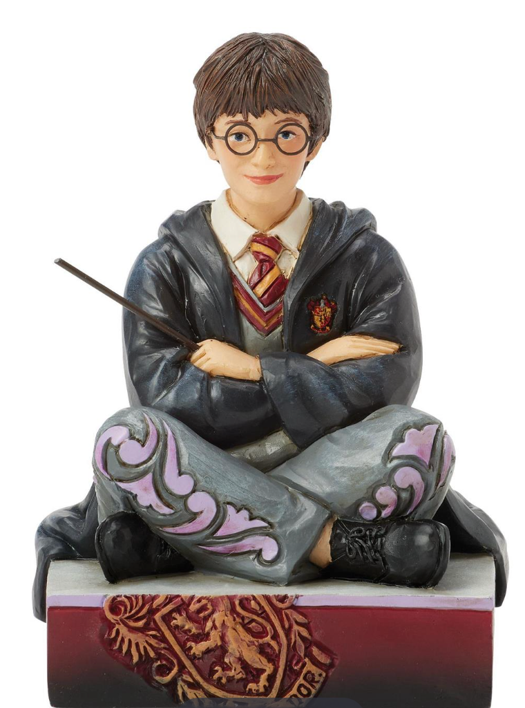Figurine of a Harry Potter in a gray robe with a wand, sitting on a decorative base.Artist Jim Shore.