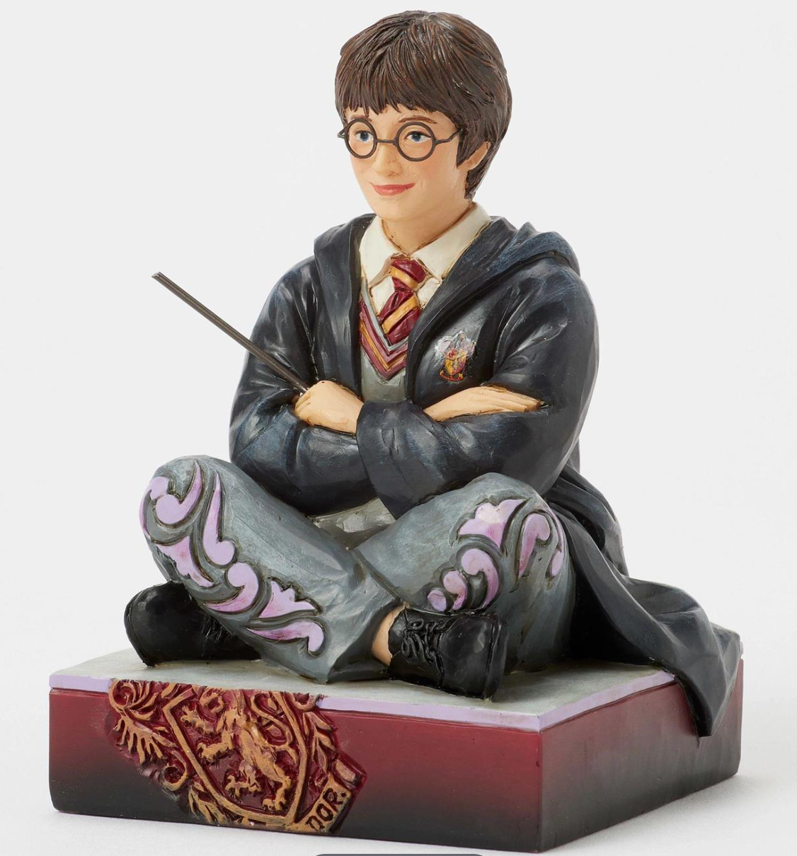 Figurine of a Harry Potter in a gray robe with a wand, sitting on a decorative base.Artist Jim Shore.