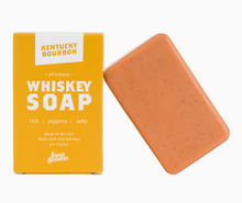 Load image into Gallery viewer, A rectangular bar of Kentucky Bourbon Whiskey Soap in a warm orange-peach color with tiny dark specks, shown next to its bright yellow packaging box on a clean white background.
