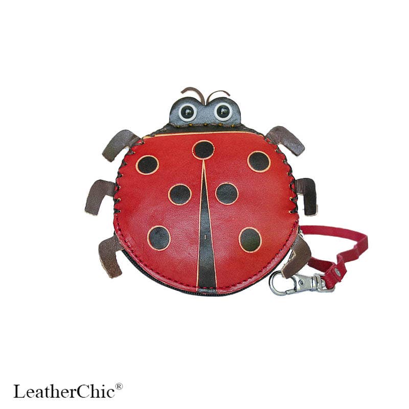 A red ladybug-shaped leather pouch with black spots, brown legs and antennae, and a matching red strap with a silver clasp, shown on a white background with the LeatherChic logo in the bottom left corner.