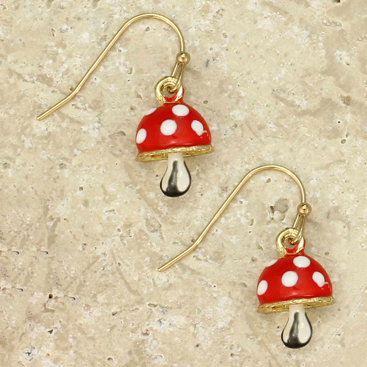 Mushroom-shaped earrings with red caps and white spots on a beige surface