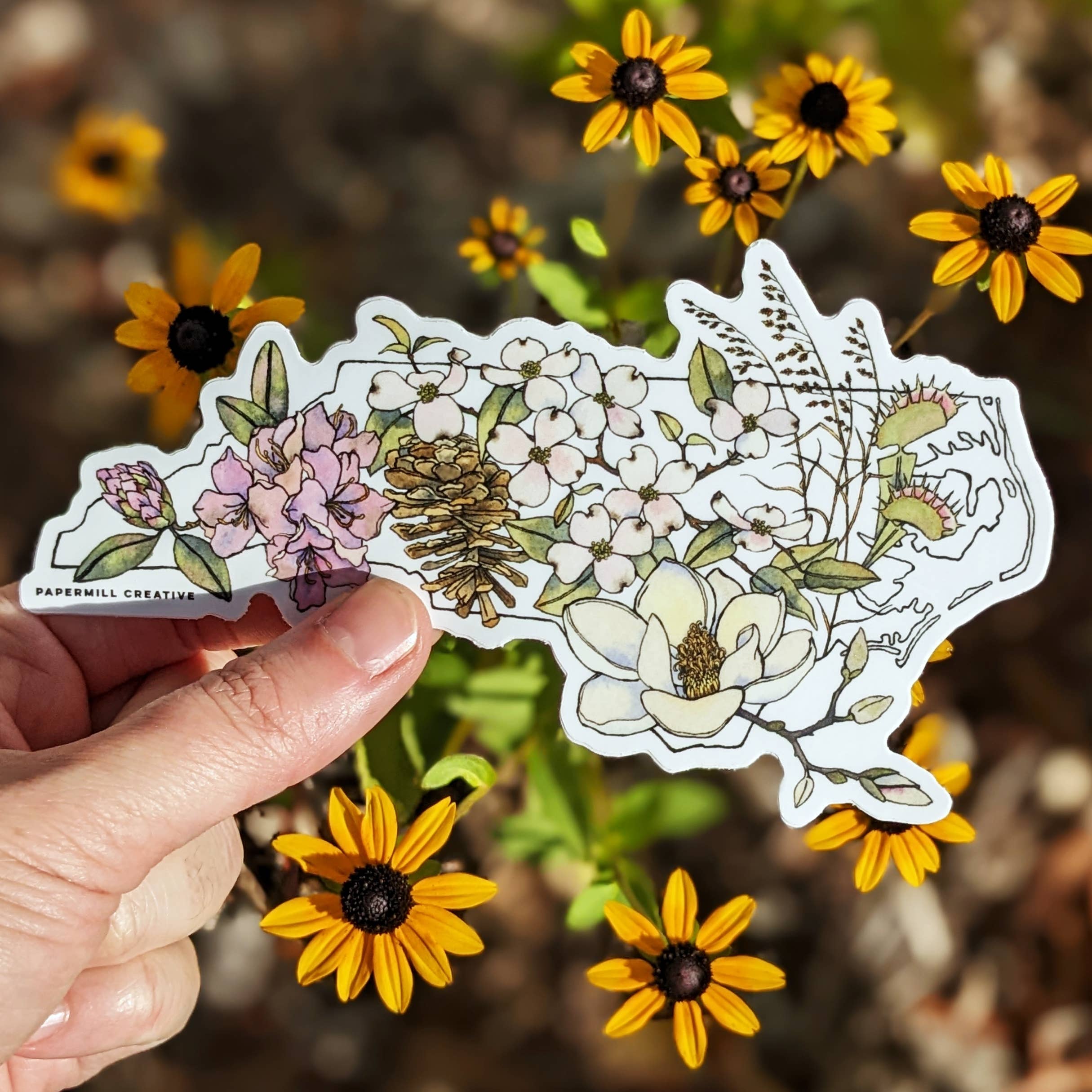 Hand holding a floral sticker with yellow flowers in the background
