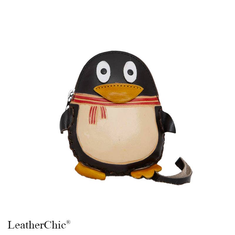 A penguin-shaped leather crossbody bag with a black body, cream belly, yellow beak and feet, and a red-and-cream striped scarf, shown on a white background with a LeatherChic watermark.