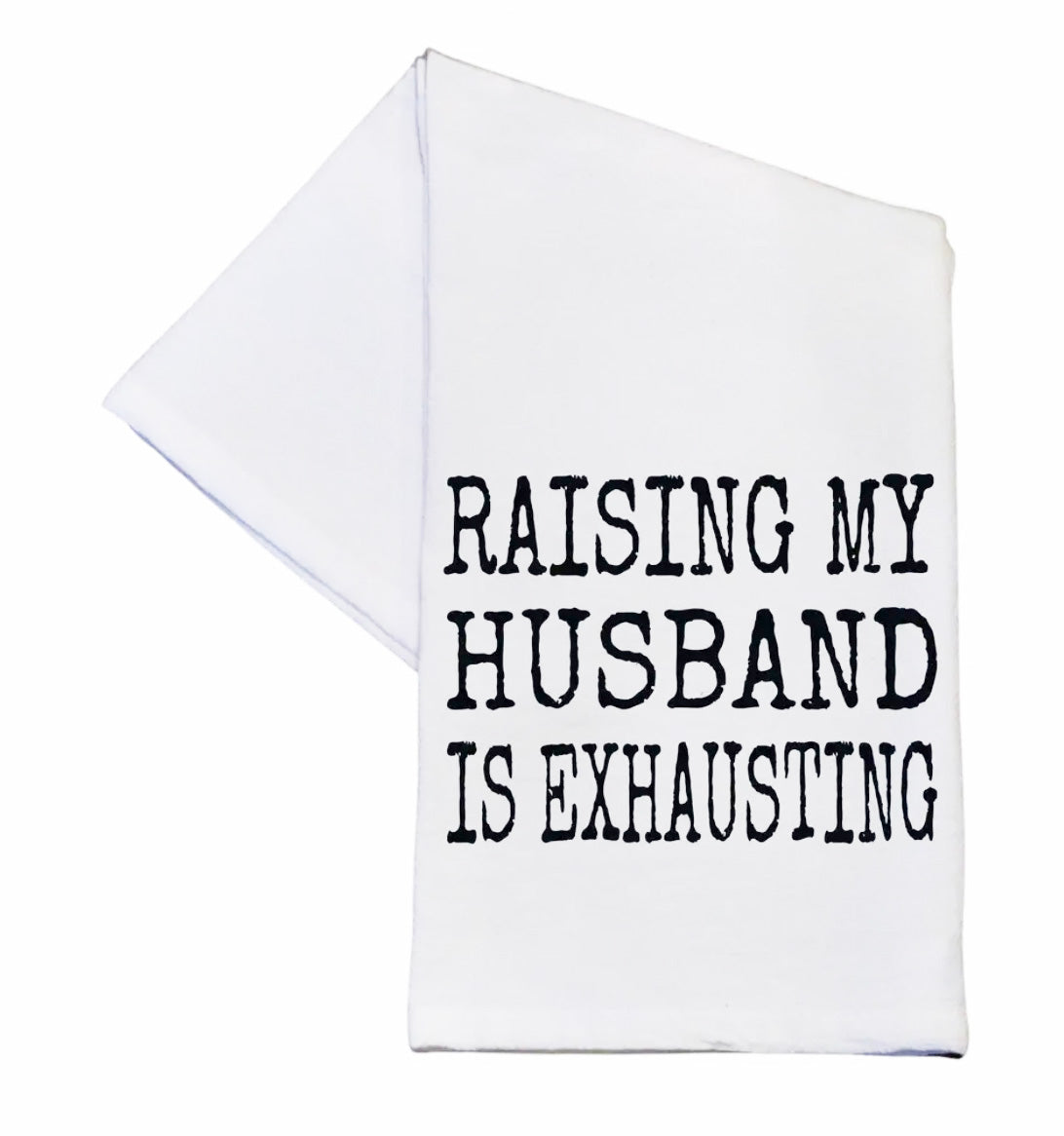 White towel with black text 'RAISING MY HUSBAND IS EXHAUSTING' on a white background