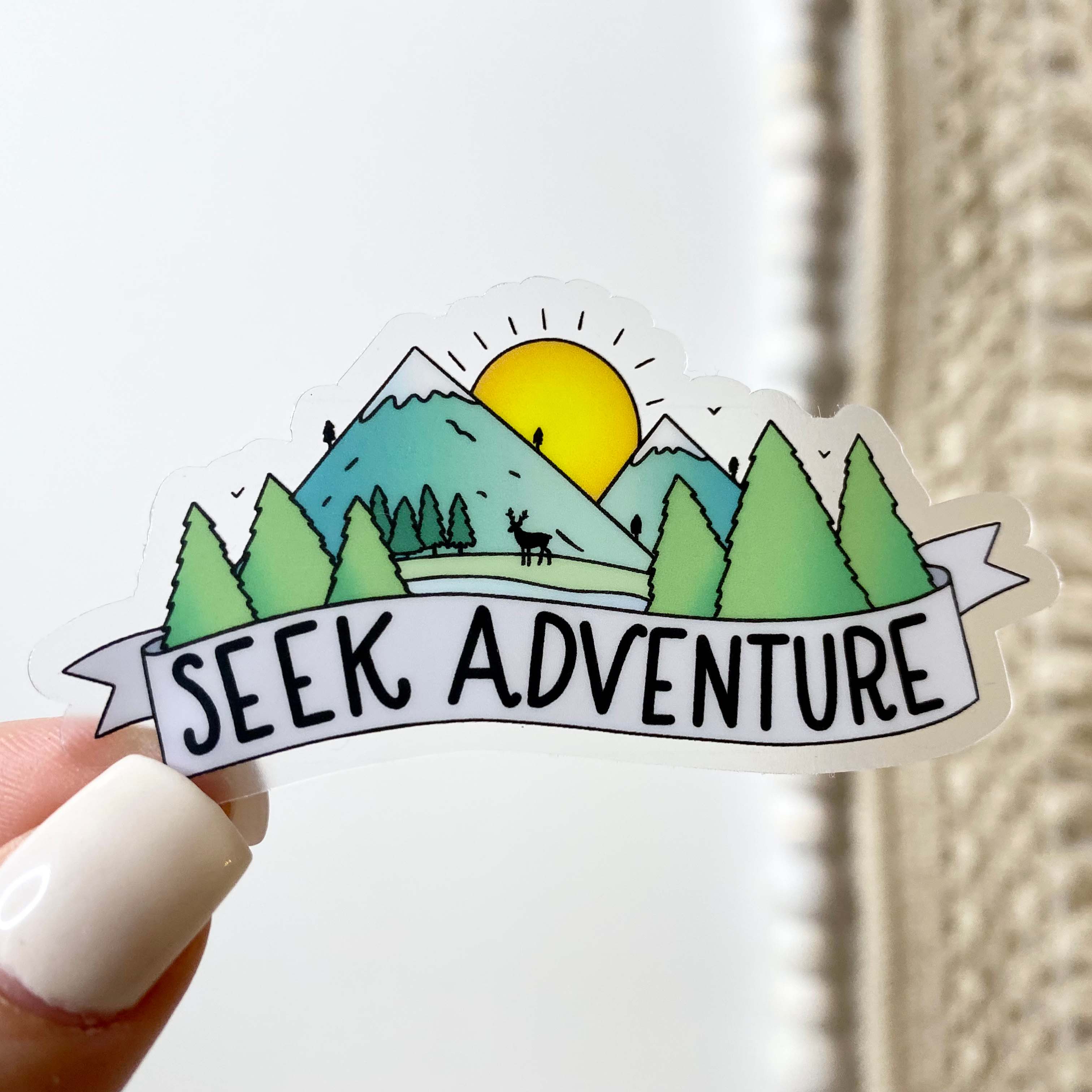 Sticker with nature design and 'Seek Adventure' text held by a hand.